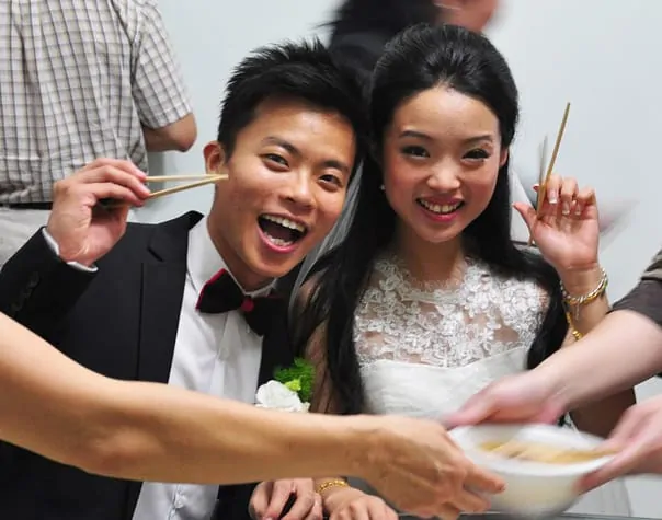 cute asian couple at their wedding holding chopsticks