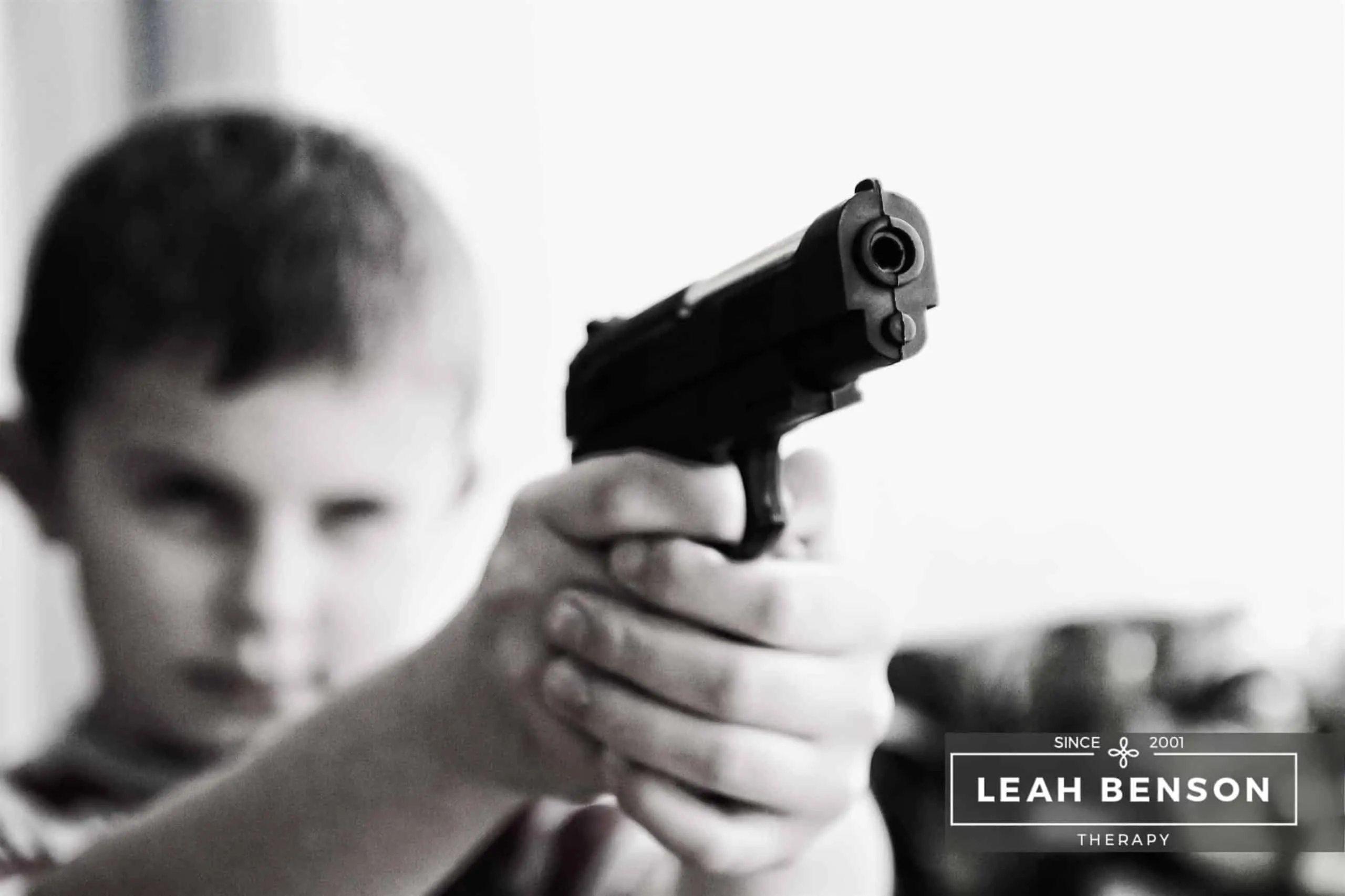 Young boy pointing a toy pistol near the camera. Text says LEAH BENSON THERAPY