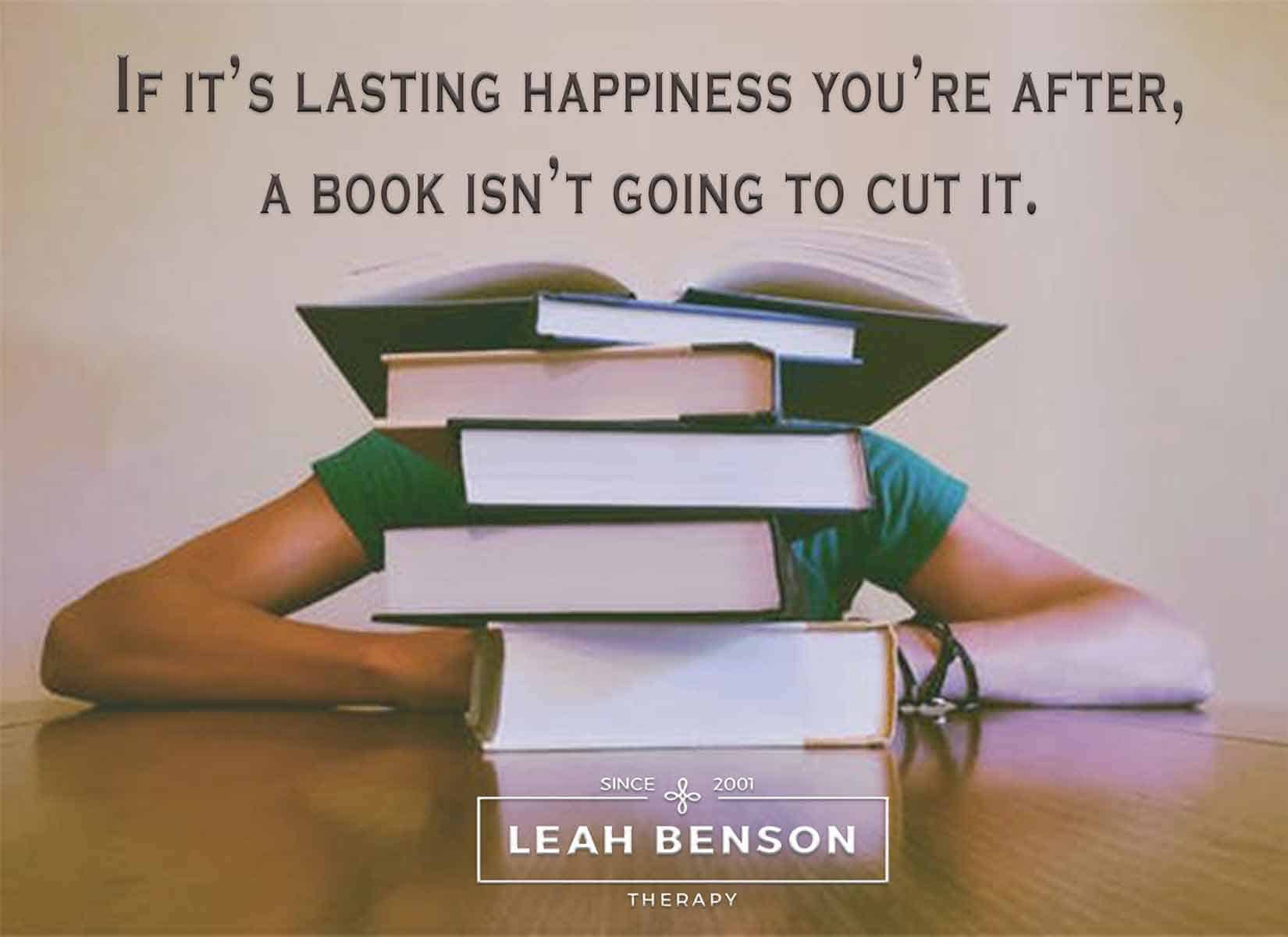 Photo of person sitting behind a stack of books with the quote, "If it's Lasting Happiness You're After, a Book isn't going to Cut It"