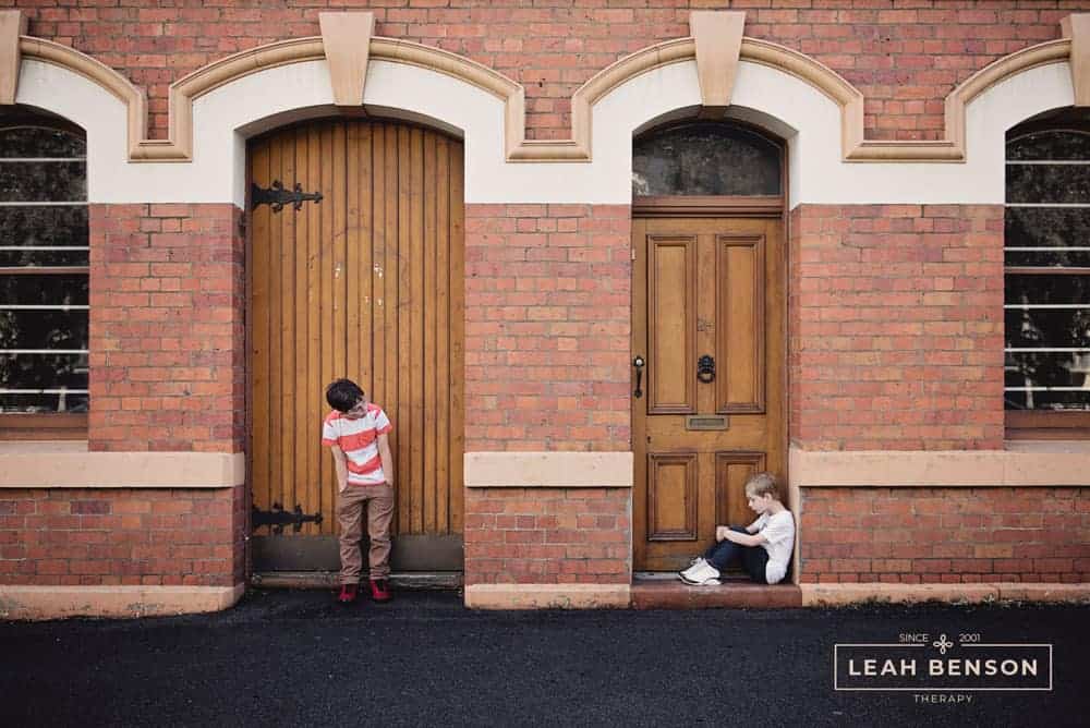 Photo by Kat Jayne of two boys, one in each doorway. Logo of Leah Benson Therapy