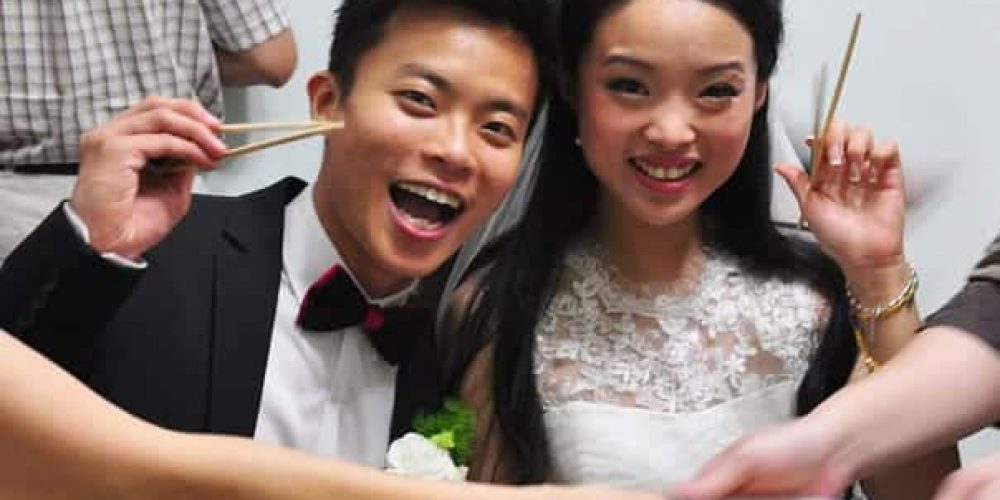 cute asian couple at their wedding holding chopsticks